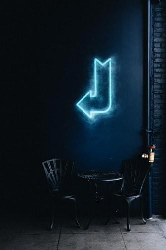 A blue neon arrow sign hanged on a wall to show a specific direction