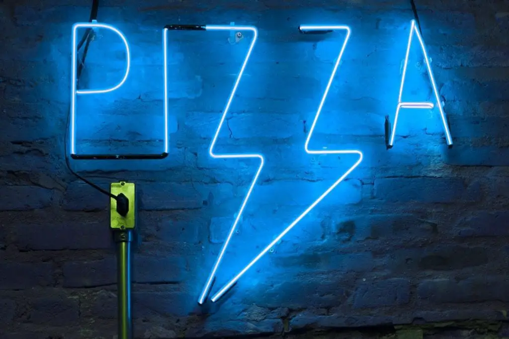 A blue neon sign in the shape of a pizza handing on a wall