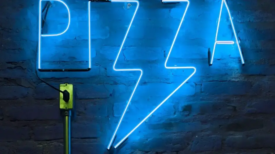 A blue neon sign in the shape of a pizza handing on a wall