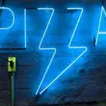 A blue neon sign in the shape of a pizza handing on a wall