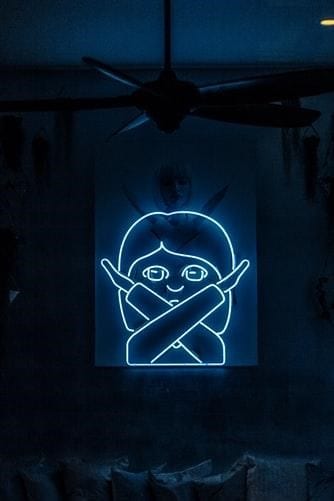 A blue neon sign of a famous emoji of a girl with crossed arms