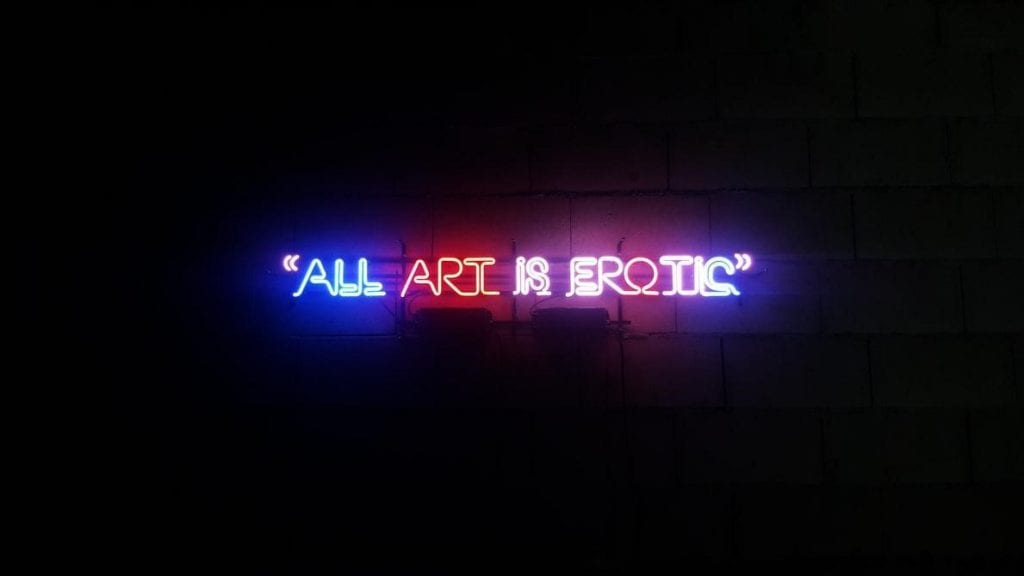 A blue neon sign with a quote about art being erotic.